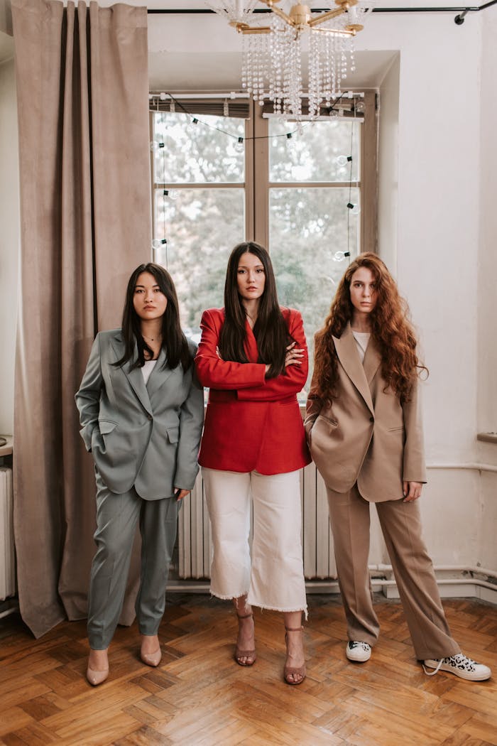 Three confident women in modern business attire standing indoors, showcasing diverse leadership.