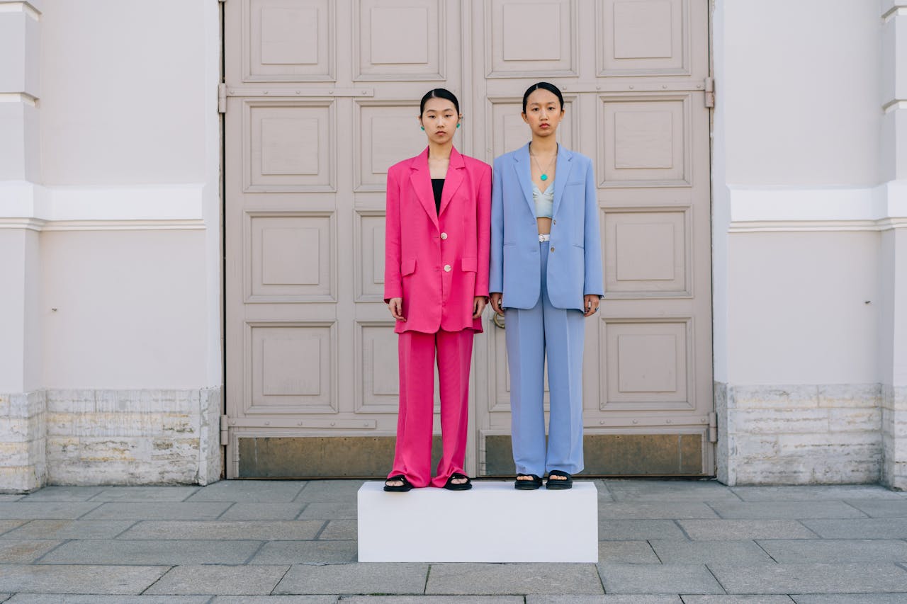 Two young women on a platform in vibrant suits, standing against a stylish backdrop.